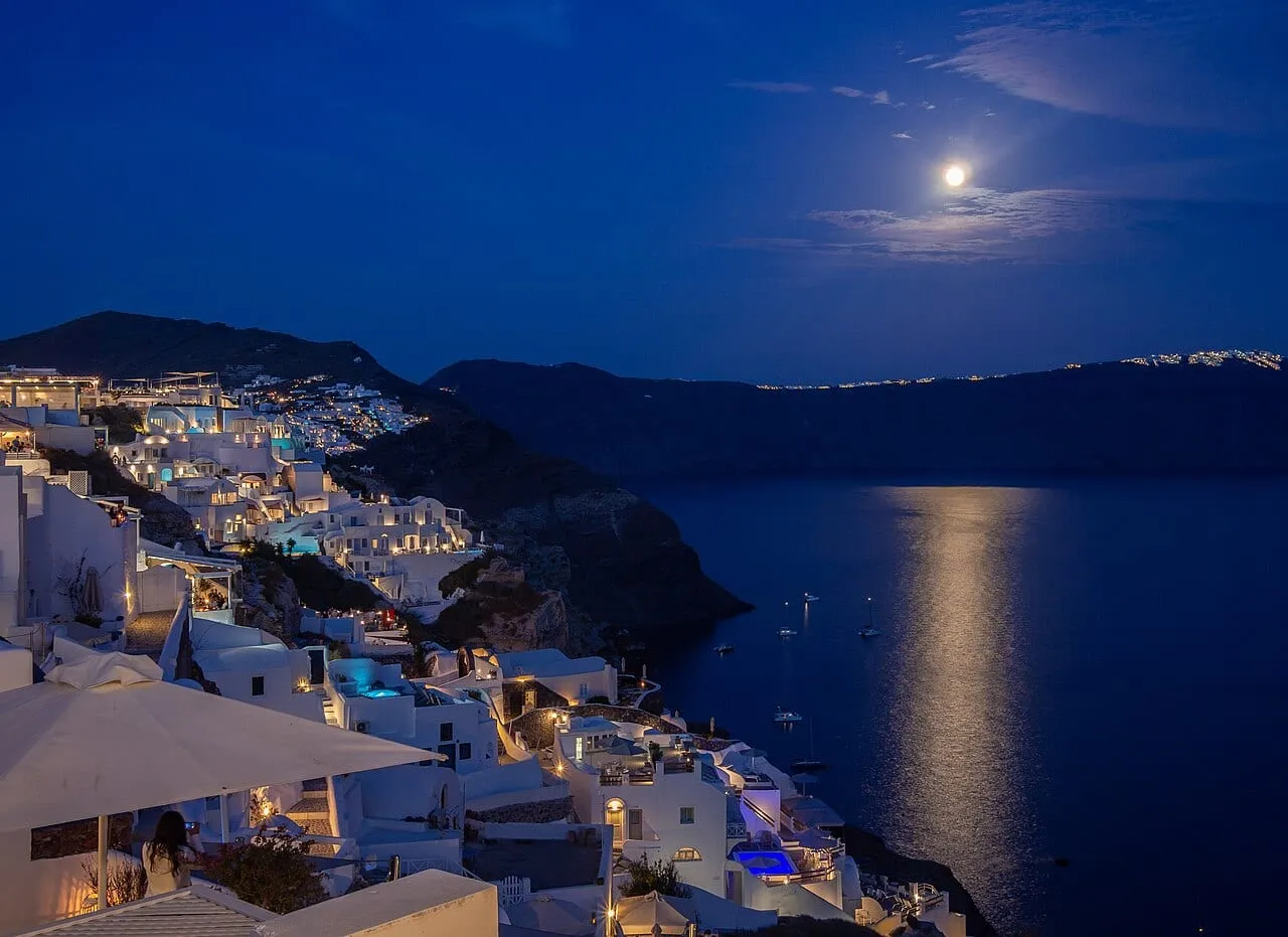 Księżyc nad Oia na Santorini i oświetlone białe domy nad kalderą