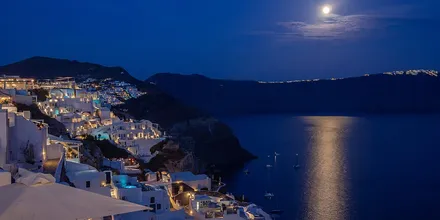 Księżyc nad Oia na Santorini i oświetlone białe domy nad kalderą