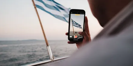 Smartfon nagrywający grecką flagę powiewającą na rufie łodzi na morzu