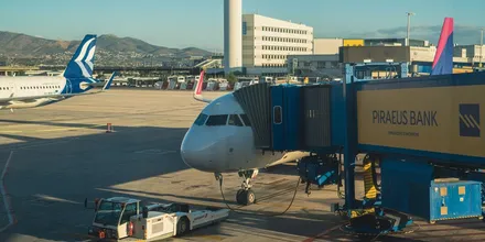 Samolot przy rękawie na lotnisku w Atenach, w tle wieża kontroli lotów i terminal
