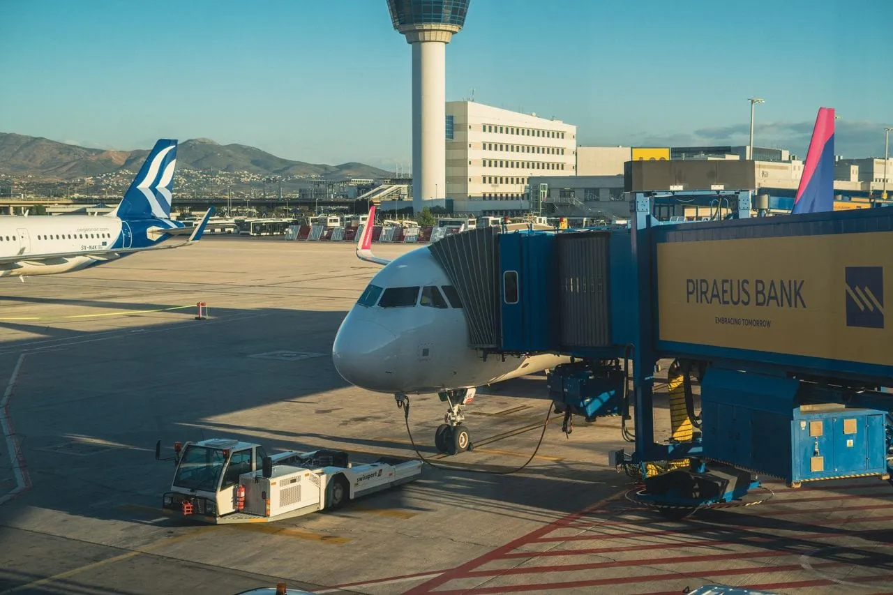 Samolot przy rękawie na lotnisku w Atenach, w tle wieża kontroli lotów i terminal
