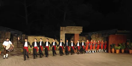 Korowód tancerzy w strojach ludowych z bębniarzem na scenie teatru Dory Stratu nocą