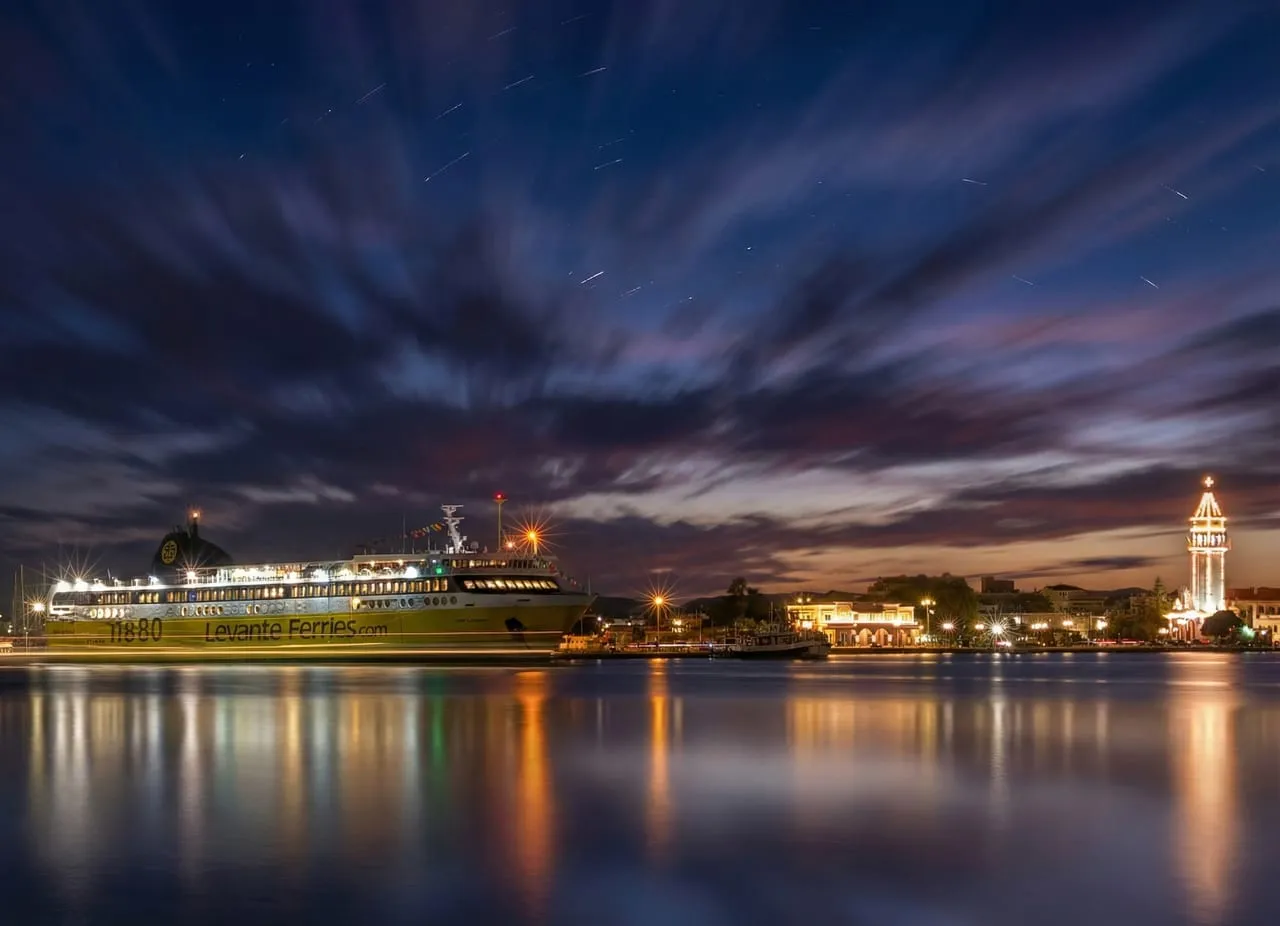 Prom Levante Ferries w porcie Zakynthos nocą, obok oświetlone nabrzeże i dzwonnica